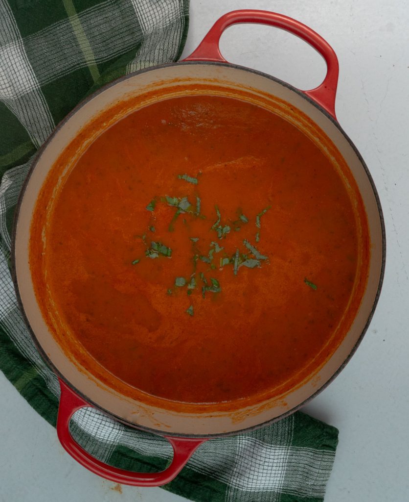 pot of roasted tomato basil soup in a red dutch oven with a green plaid kitchen towel off to the left