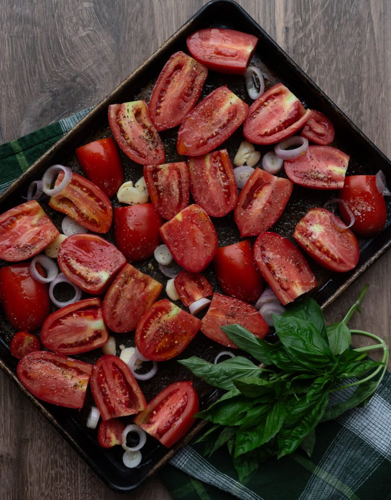 roma tomatoes on a baking sheet with garlic, shallot, olive oil, salt and pepper