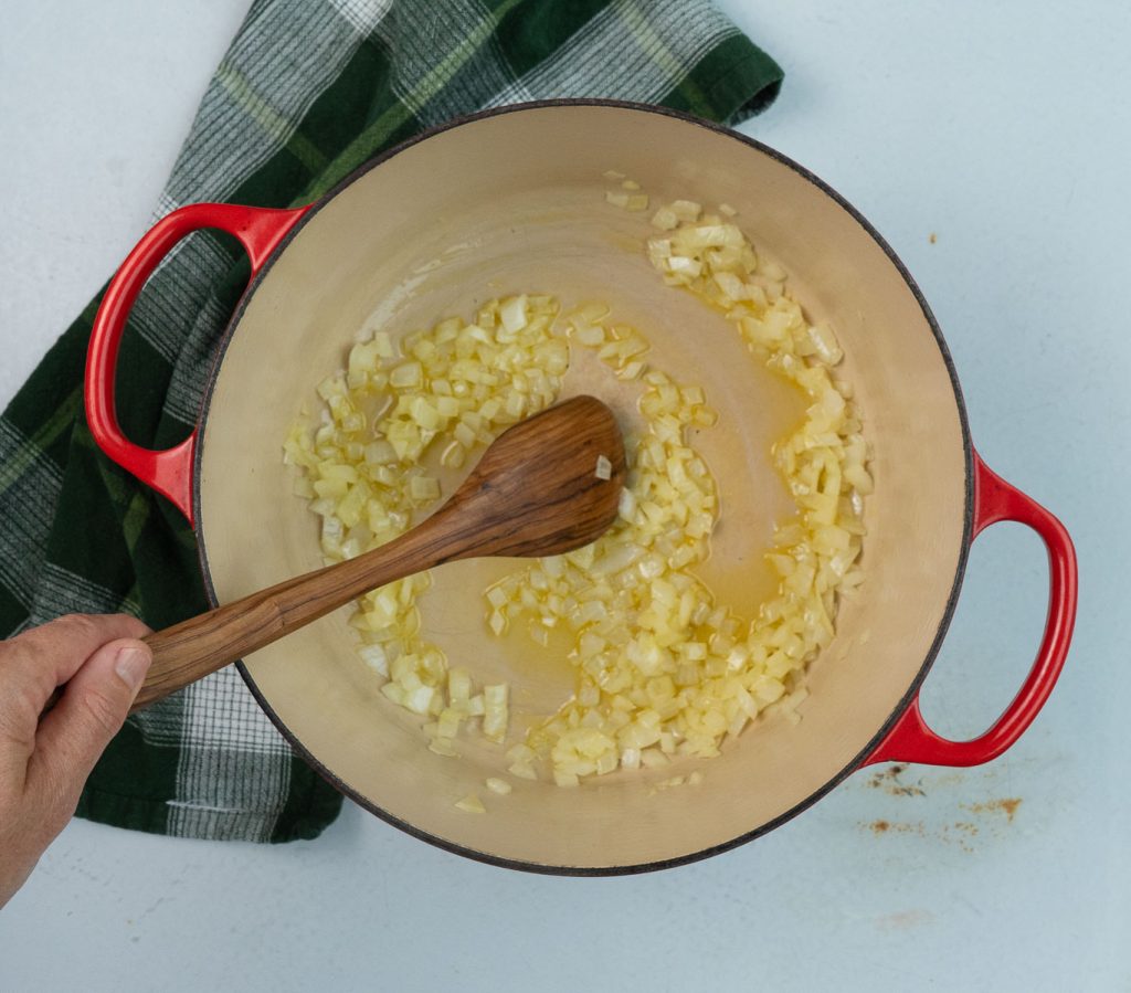 onion sauteing in dutch oven with a wooden spoon stiring