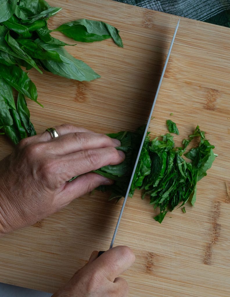 basil being chopped on a wooden cutting board