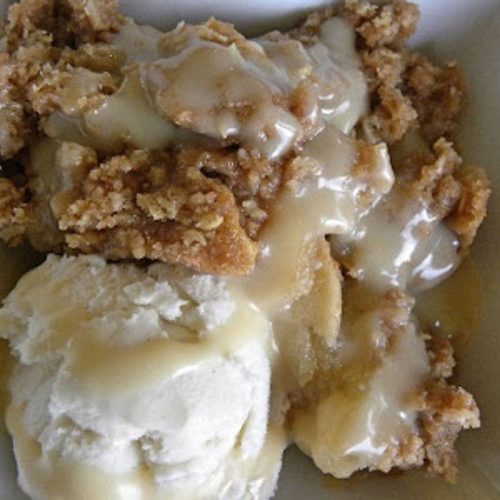 apple crisp in a white dish with a scoop of vanilla ice cream on top