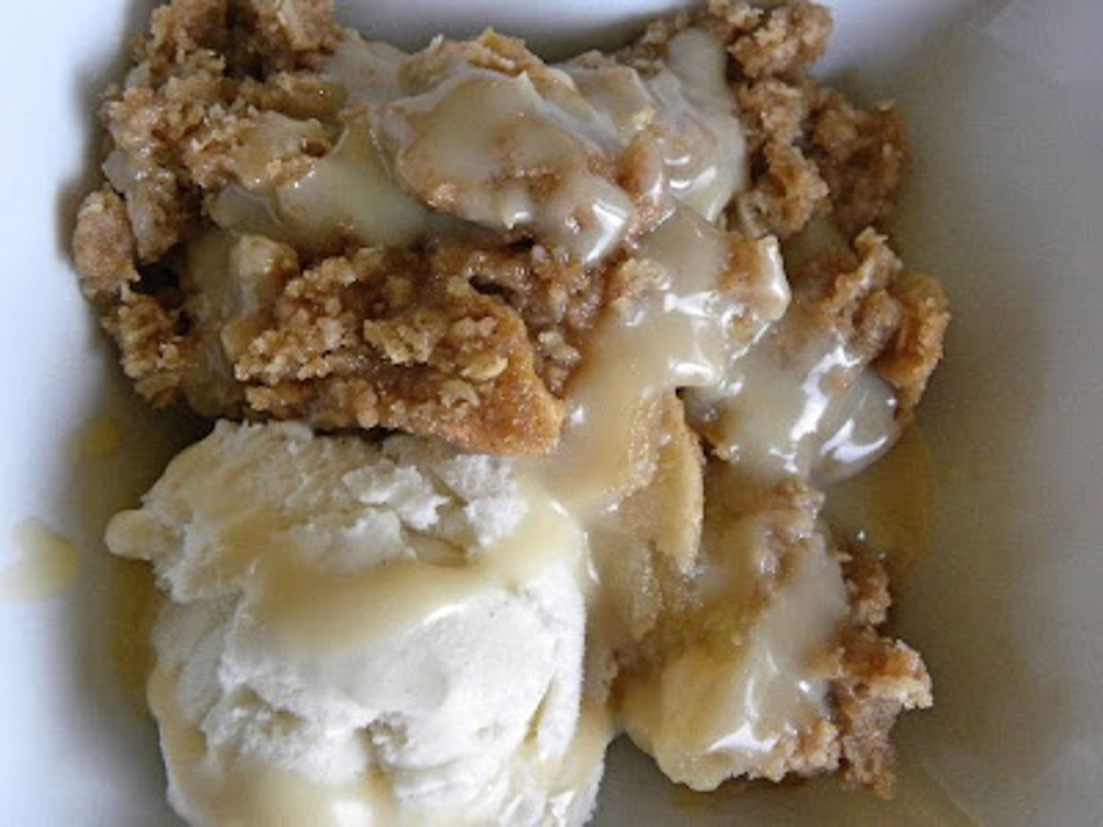 apple crisp in a white dish with a scoop of vanilla ice cream on top