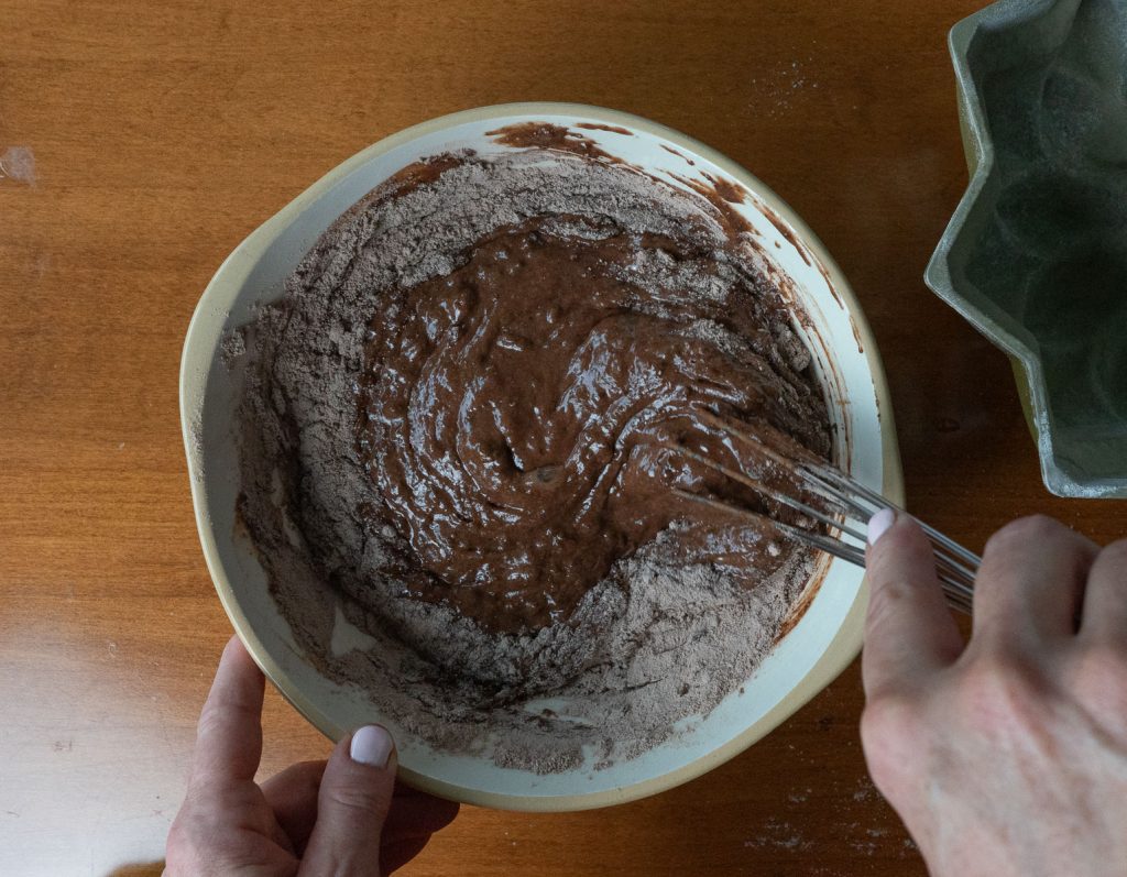 Stirring batter in a glass bowl with a whisk on a wood counter top. 