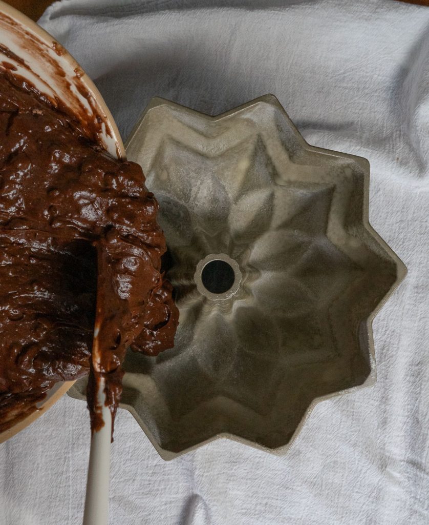 pouring chocolate cake batter into prepared bundt cake pan 