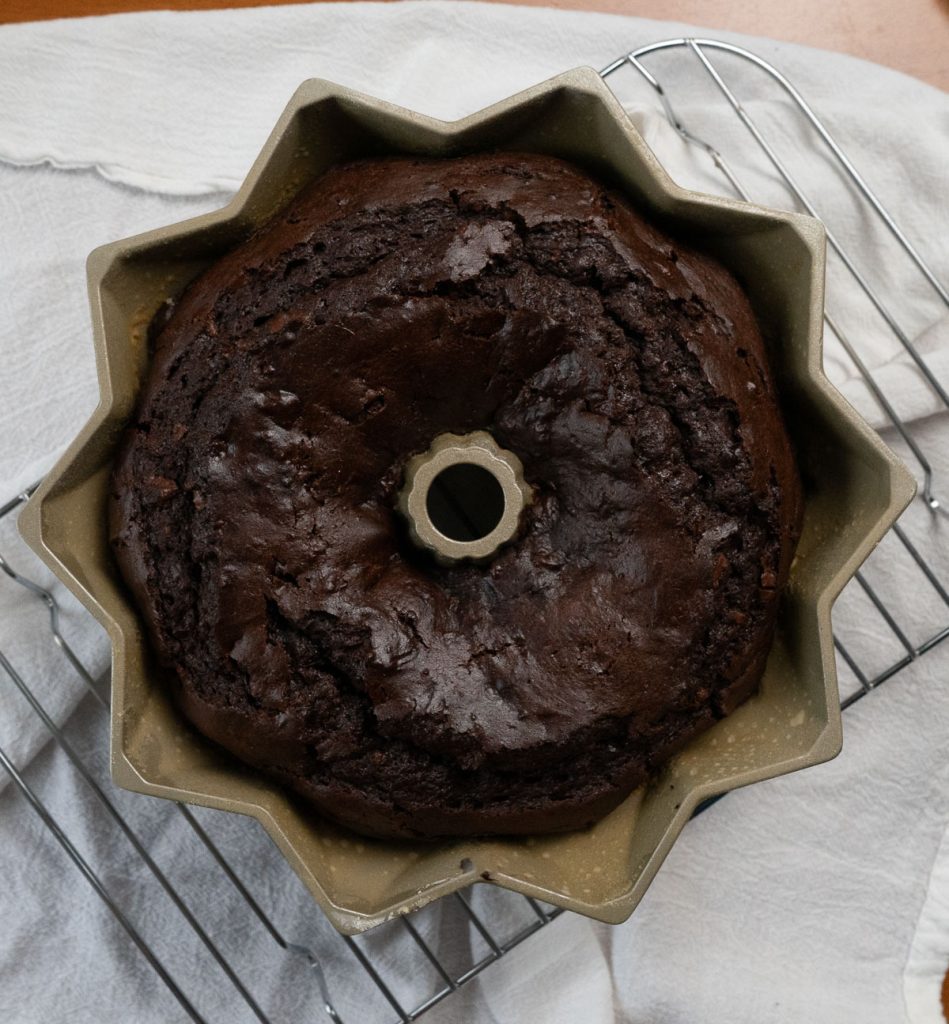 triple chocolate bundt cake baked in pan, pan is sitting on cooling rack on a white cloth