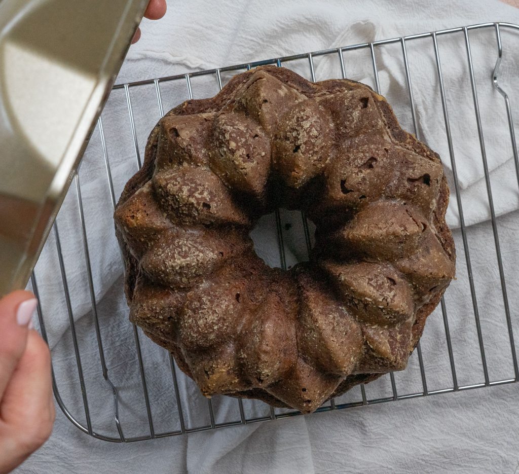 triple chocolate bundt cake cooling on rack white cloth spread out underneath cake and rack