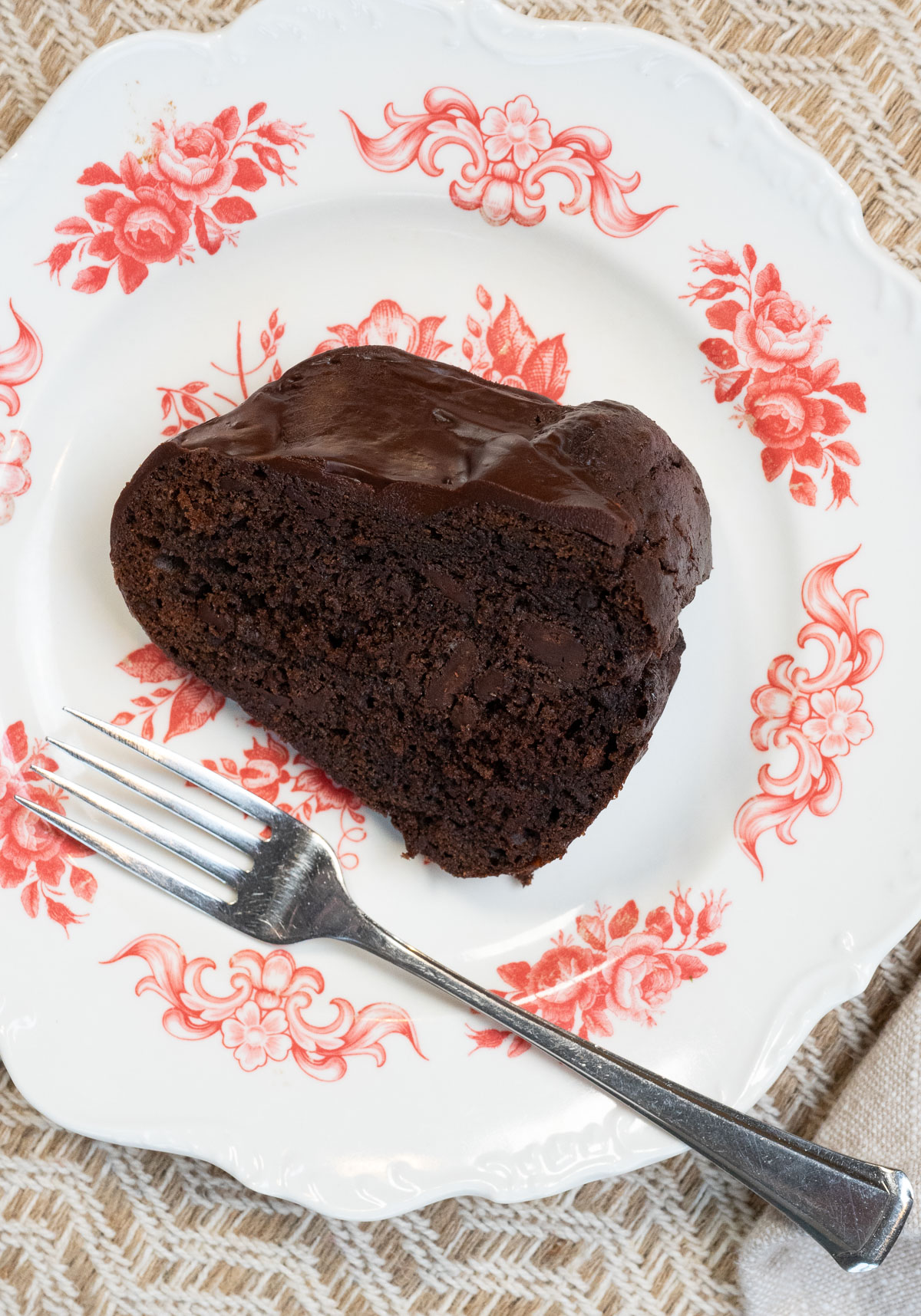 one piece of dark chocolate cake on a white plate with floral design around the edge and a fork laying across the bottom