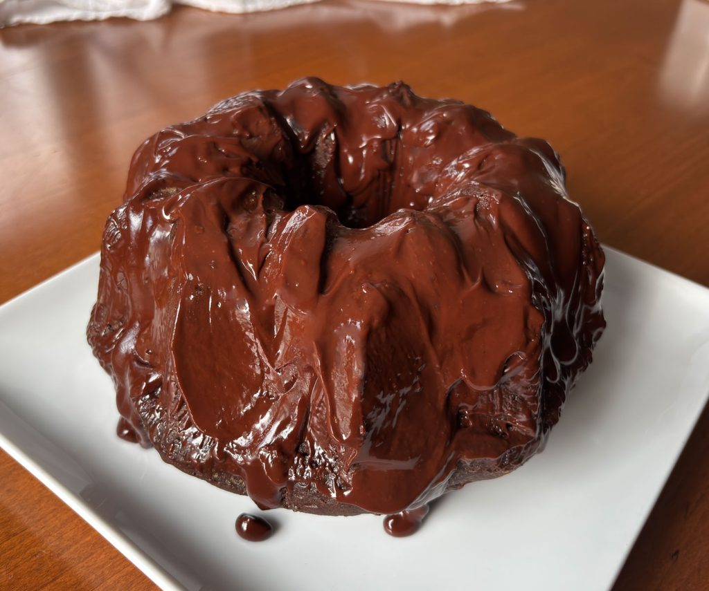 Triple Chocolate Bundt cake on a white cake plate on a wood table