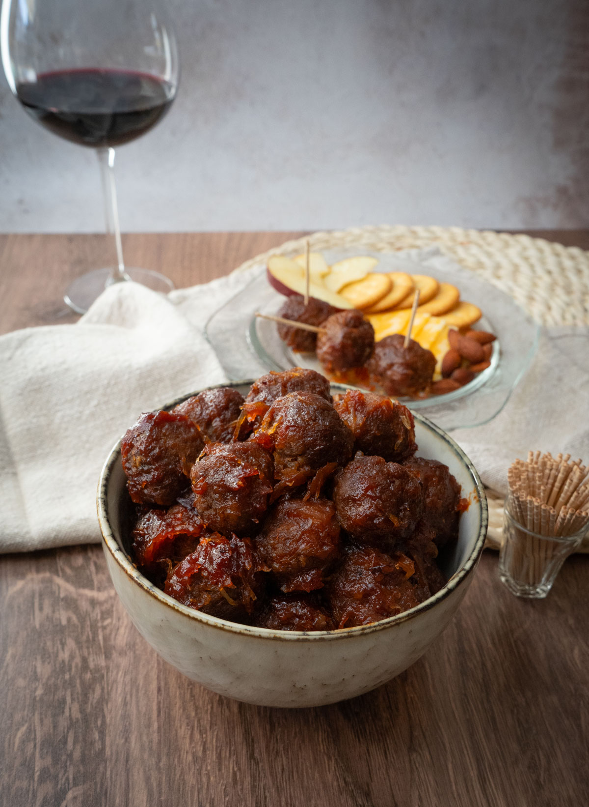 table with appetizer meatballs, a plate of appetizers and a glass of red wine