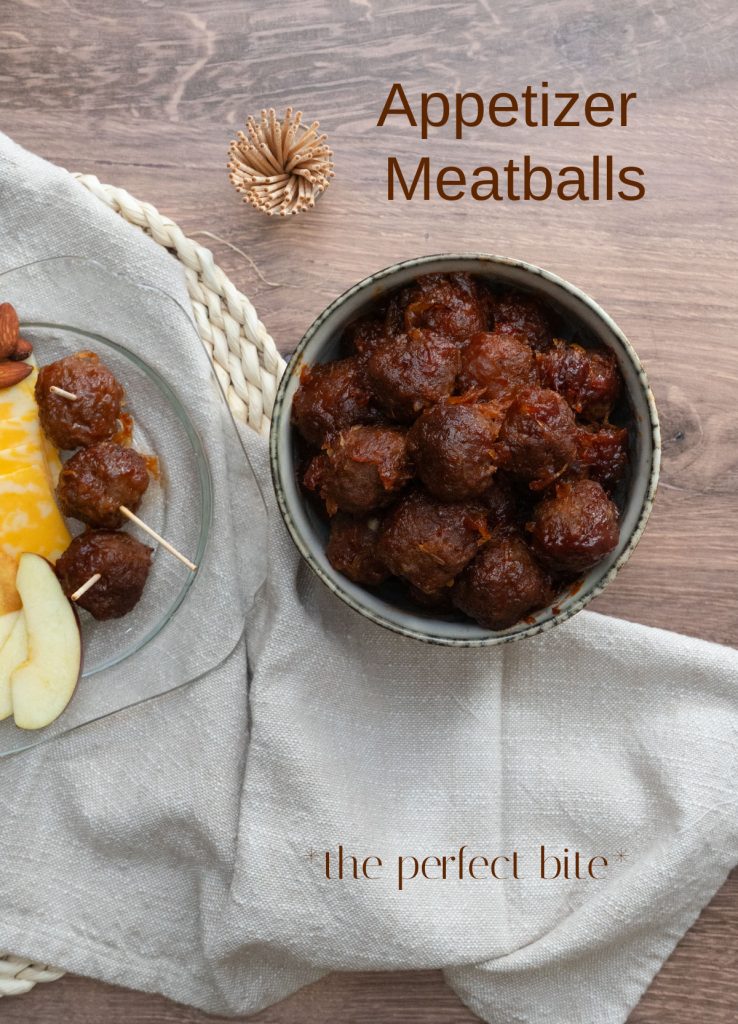 appetizer meatballs in a bowl on a wood countertop with cocktail toothpicks in a glass cup above, and a place of different snacks off the the left