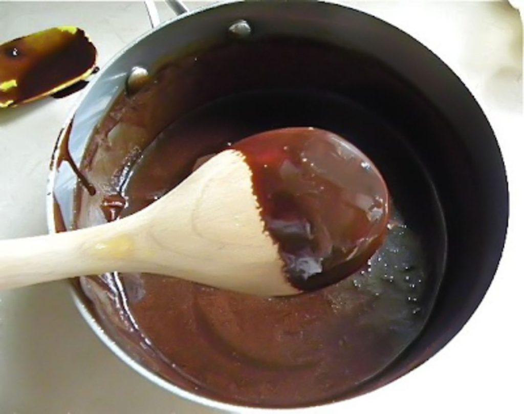 wooden spoon with fudge covering the back of it.  over a sauce pan of no bake cookie fudge