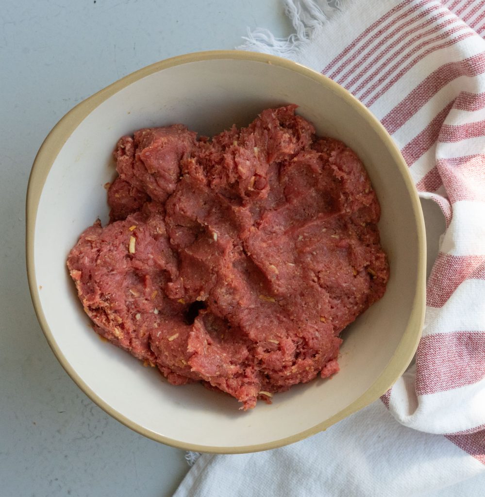 meatball mixture in a large bowl on a white countertop with a kitchen towel laying to the right of the bowl