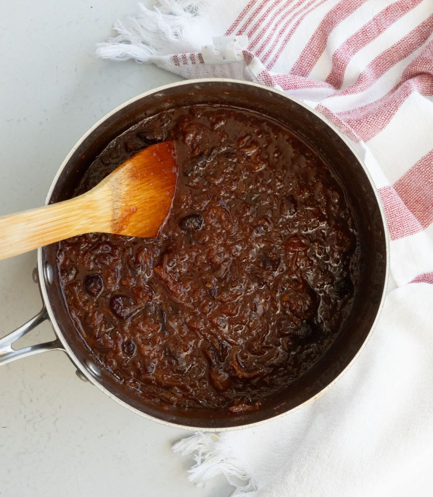 fully cooked appetizer meatball sauce in a sauce pan on a gray background with a kitchen towel off to the right side of the pan