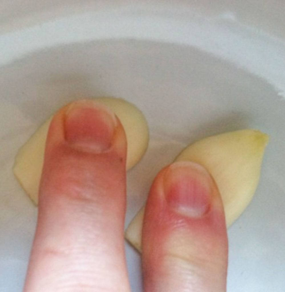 two fingers pressing garlic cloves into the bottom of fondue pot. 