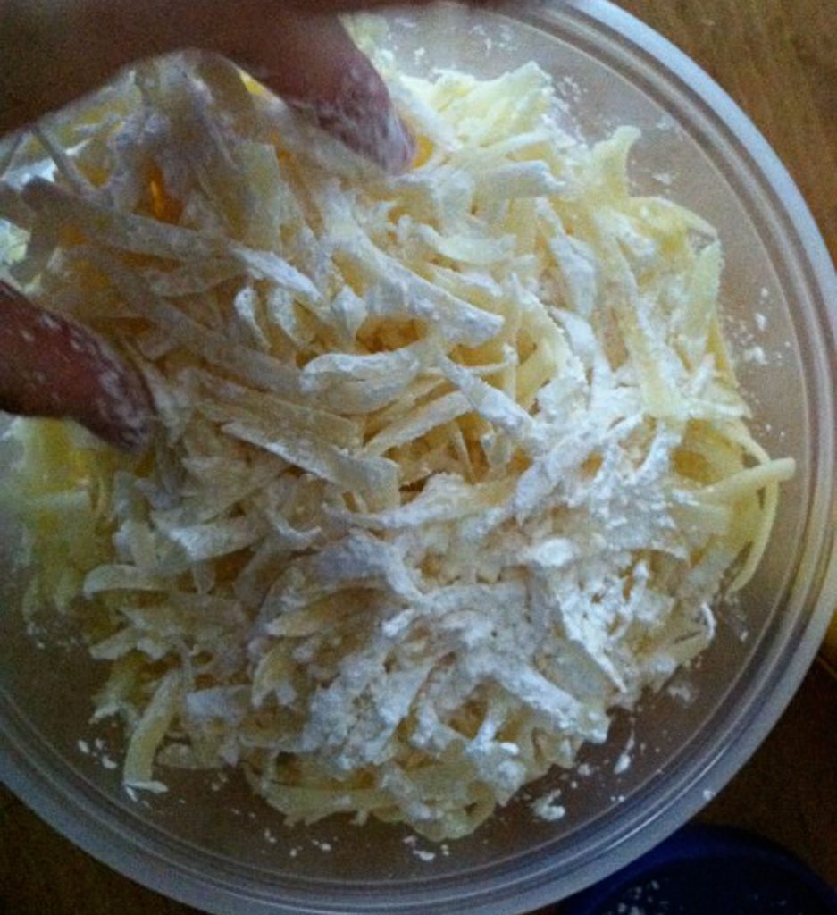 grated cheese being tossed with cornstarch in a plastic bowl