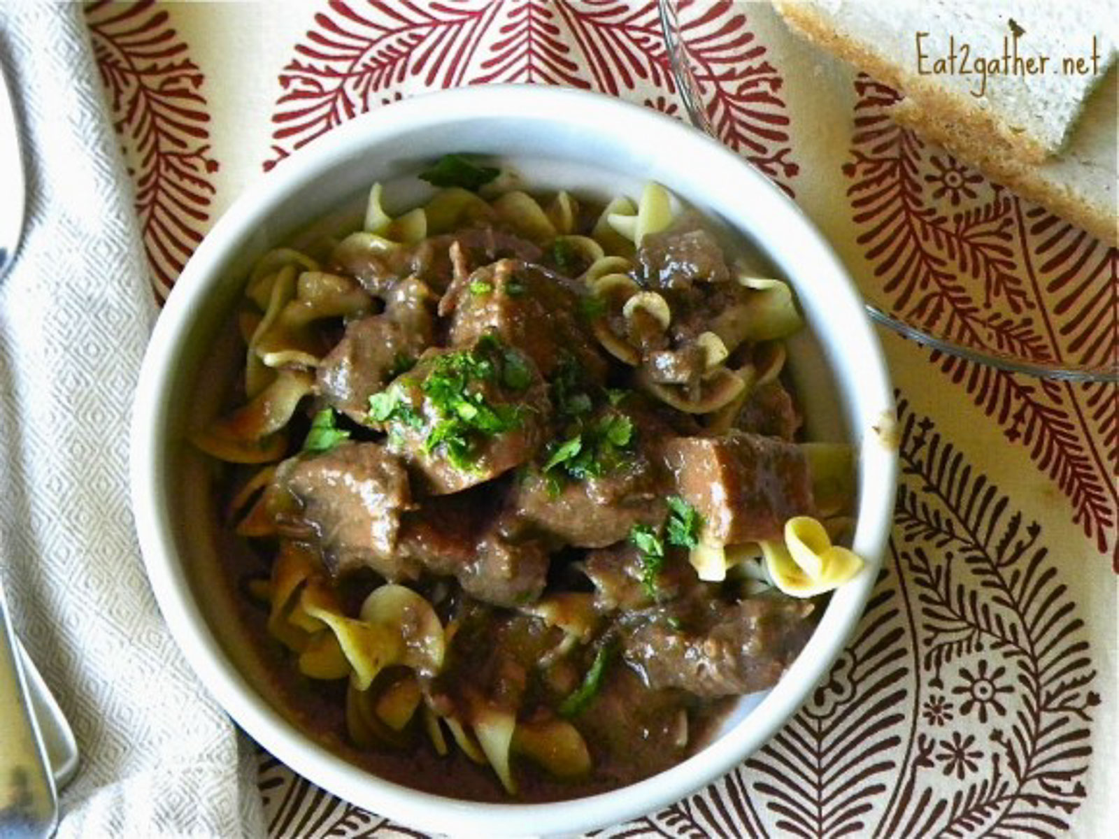 beef stew over wide egg noodles in a round white bowl on a place matt