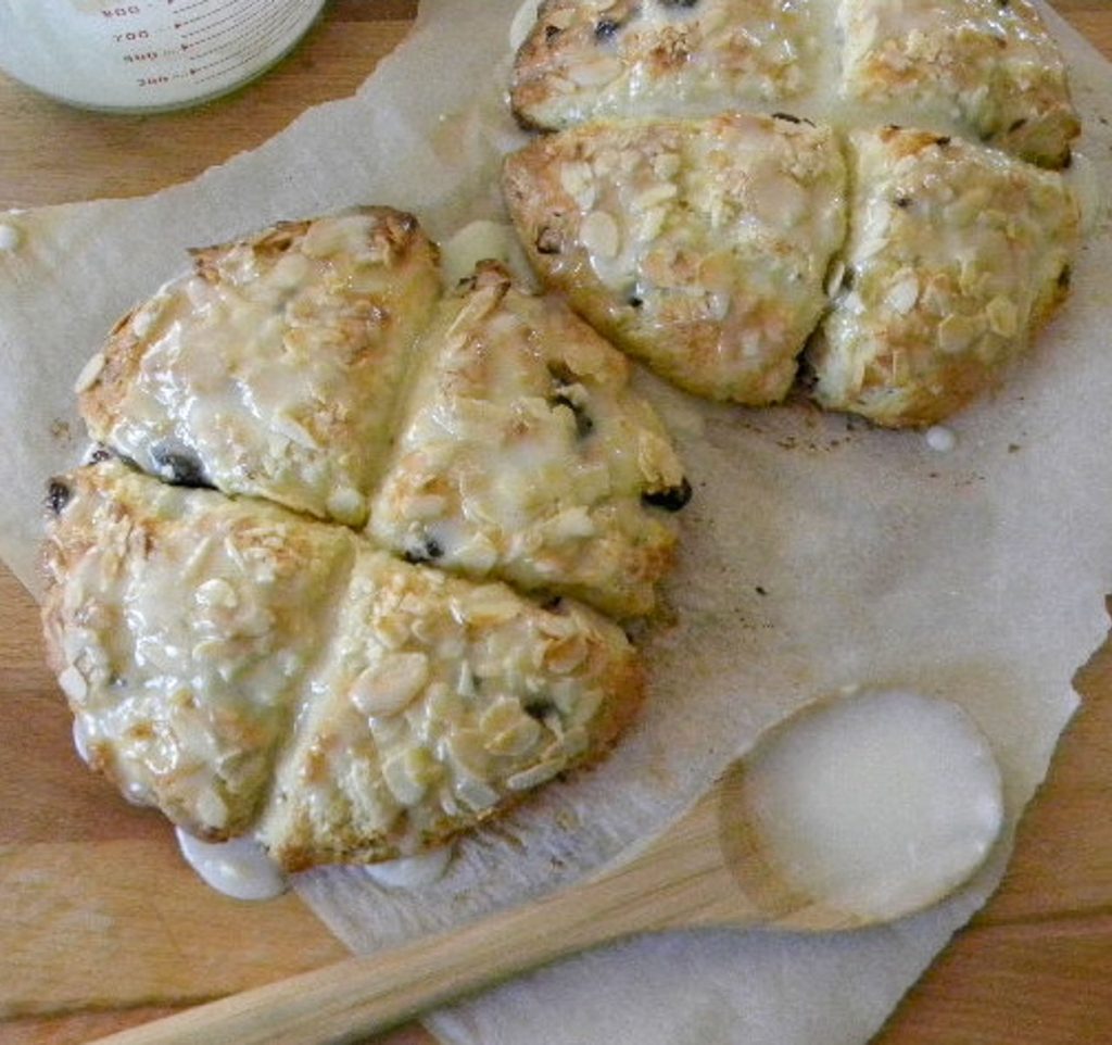 cherry almond scones on parchment paper with a wooden spoon in the lower section of the photo with icing on it