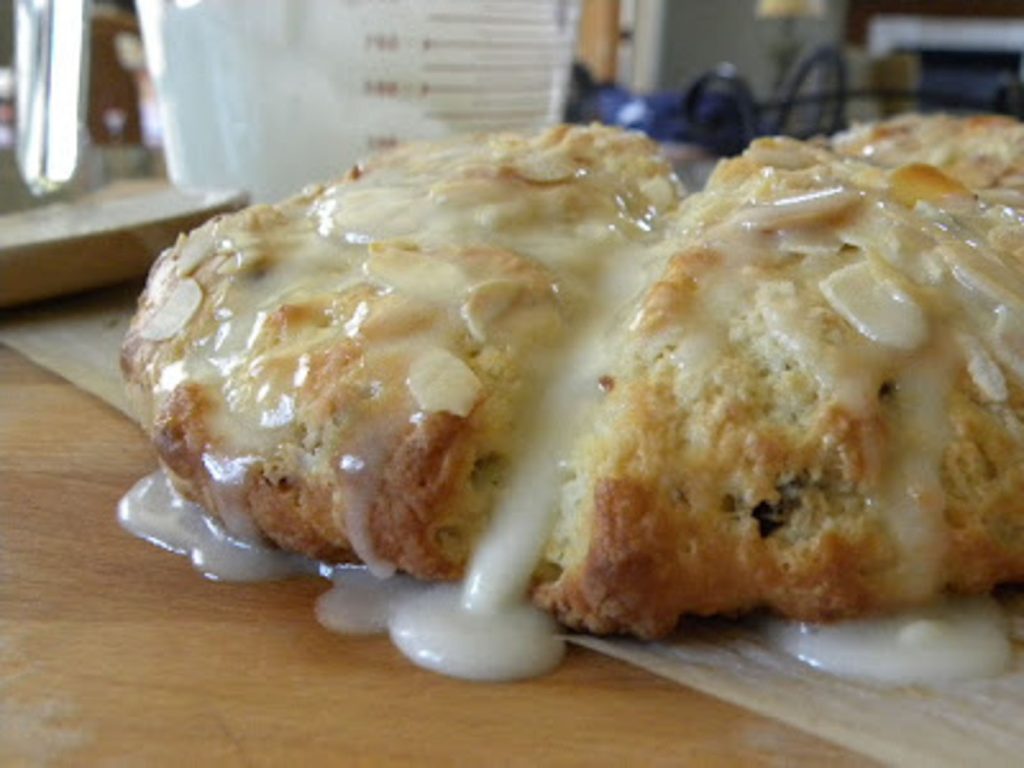 Cherry Almond Scones dripping with almond icing on parchment paper and wood cutting board