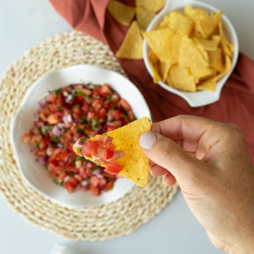 corn tortilla chip with pico de gallo on it with a bowl of pico de gallo and a bowl of tortilla chips in the background