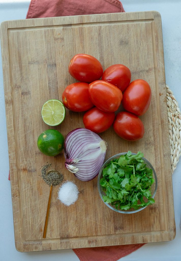 tomatoes, lime, onion, cilantro, salt and peppper: ingredients for pico de gallo on a wood cutting board