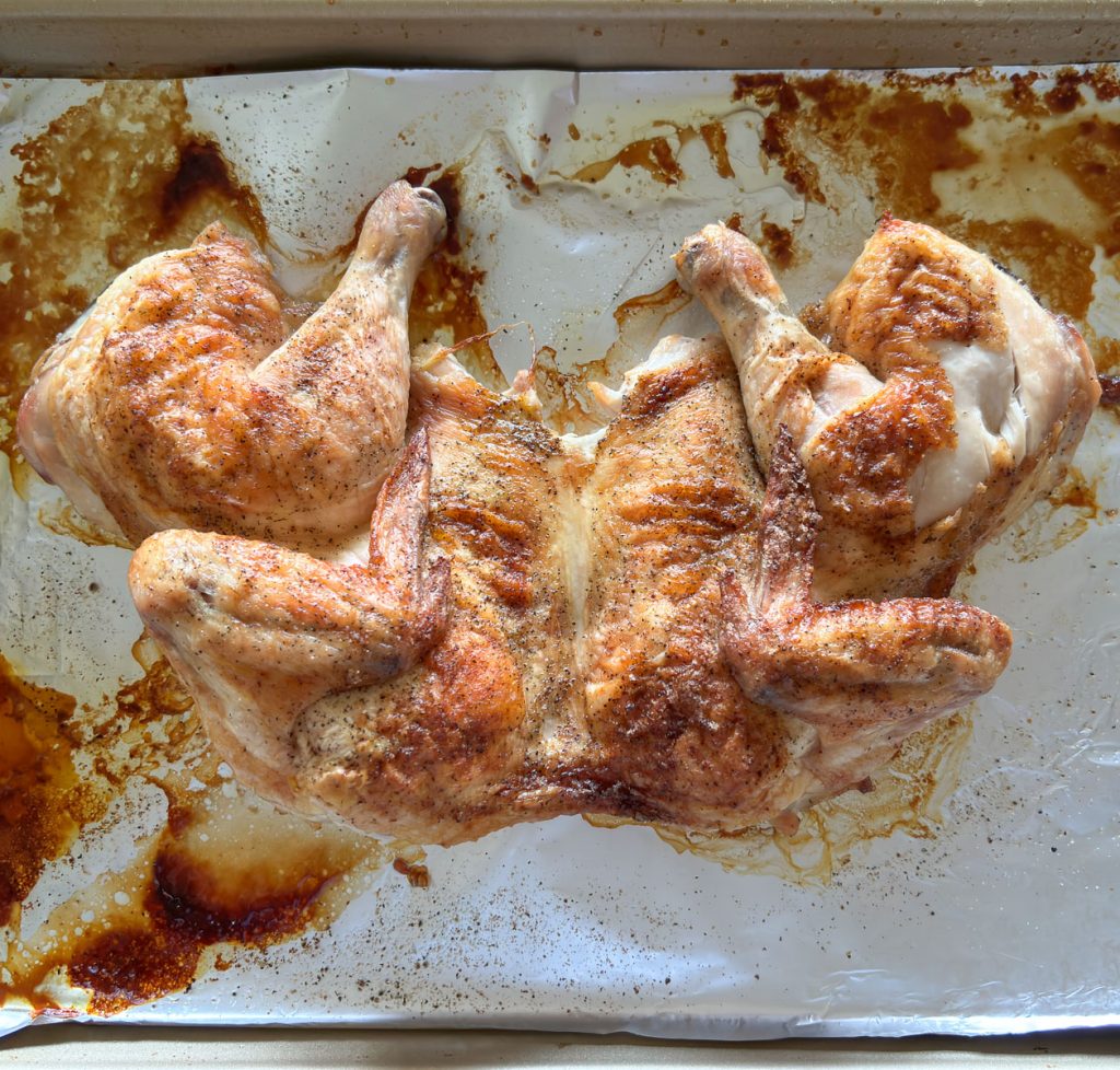 photo of a roasted spatchcock chicken on a aluminum foil covered baking sheet