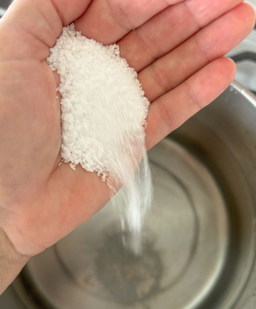 hand pouring salt in a boiling pot of water, preparing for boiling pasta 