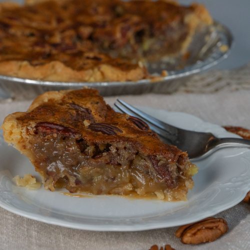 slice of pecan pie on a white plate with a whole pie in the background