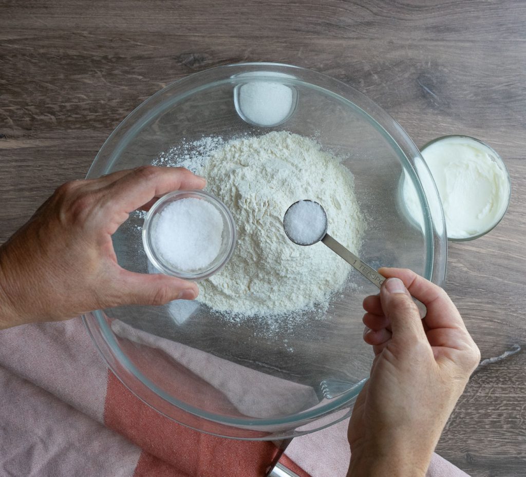 mixing dry ingredients for pie crust in a glass bowl on a wood counter top