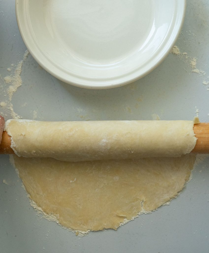 pie crust rolled out onto a  gray countertop. rolling pie dough over the rolling pin. pie dish sitting above rolling pin