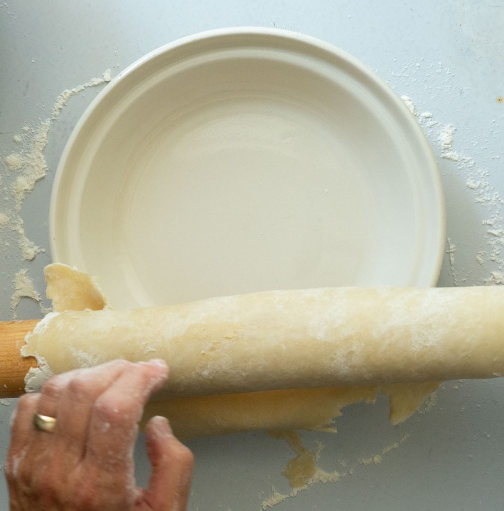 picking up rolling pin and rolling pie crust over pie plate 