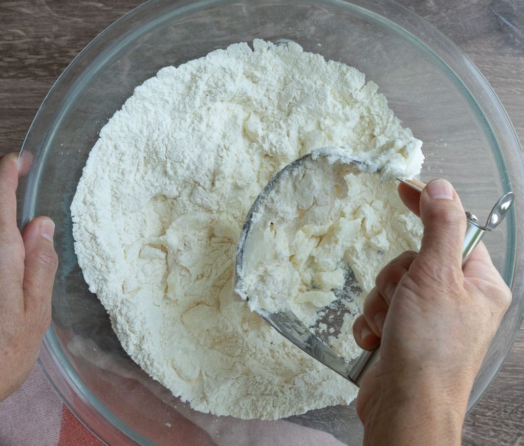 add fat to the dry ingredients for pie crust, in a glass bowl, hand is using a pastry cutter to cut the shortening / butter into dry ingredients 