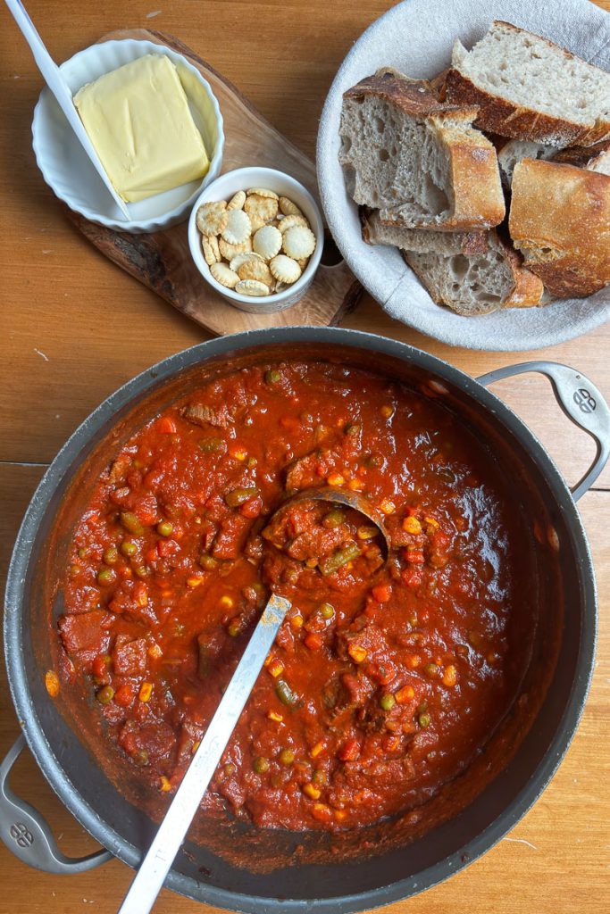 pot of steak soup on a table with a basket of bread, butter, and soup crackers