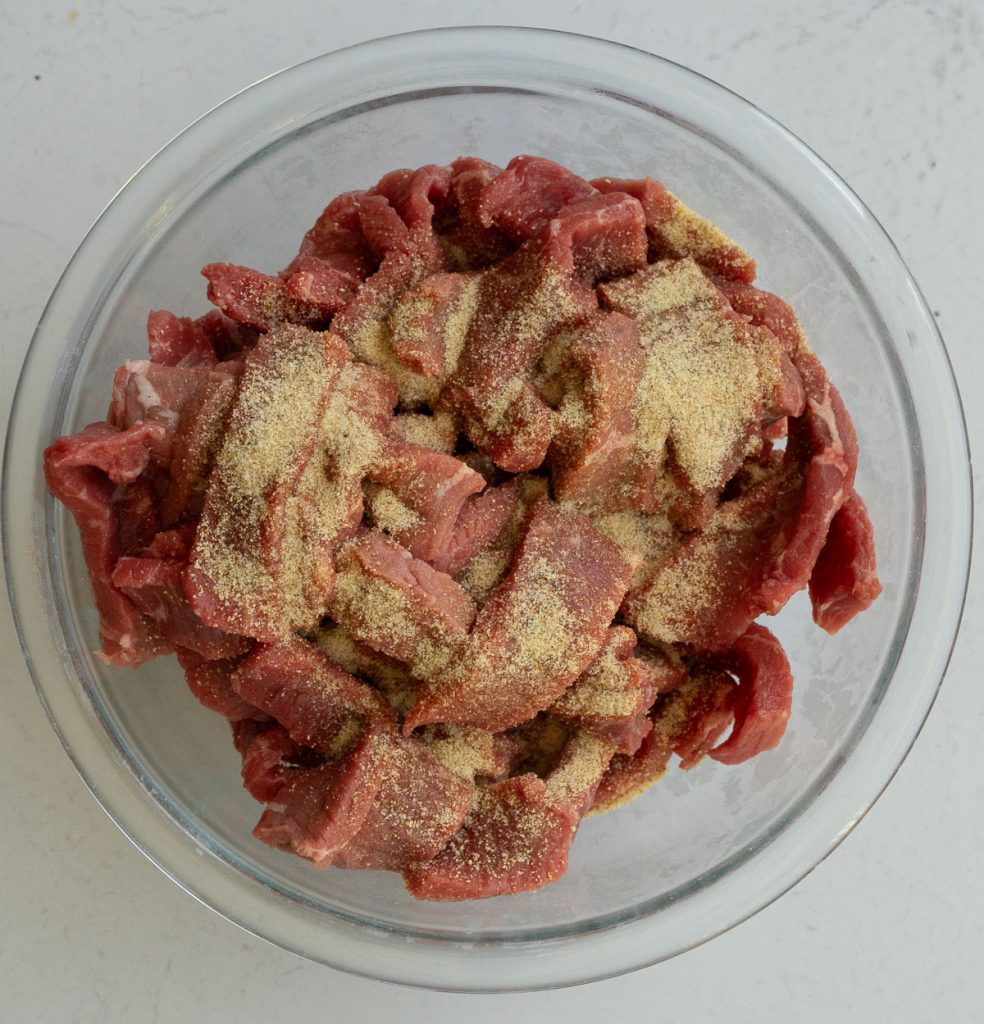 sliced steak in a glass bowl sprinkled with lawrys salt 