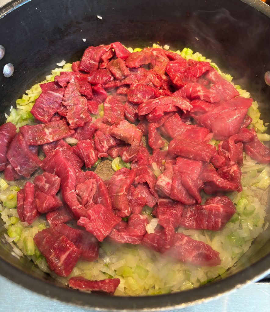 Adding seasoned steak strips to the saute'd onions and celery in large pot on stove top