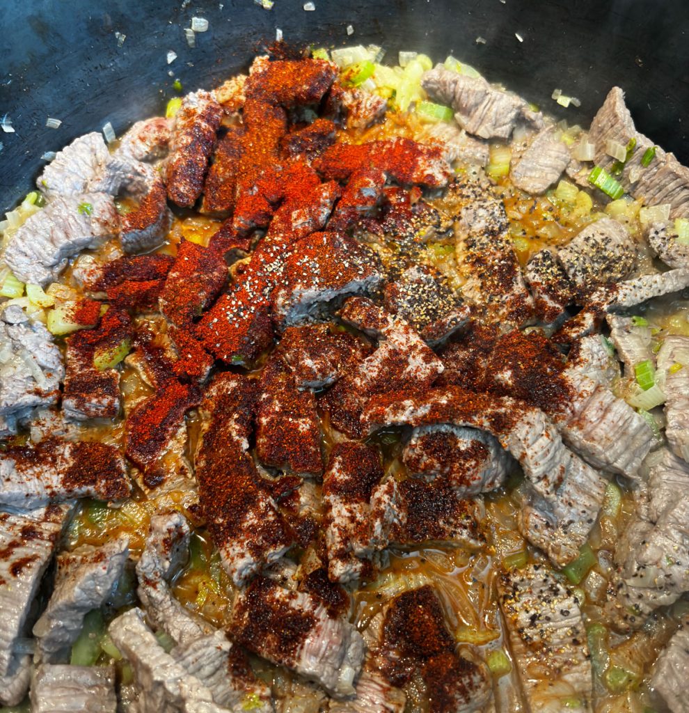 onion, celery, and steak in soup pot with spices sprinkled over the steak