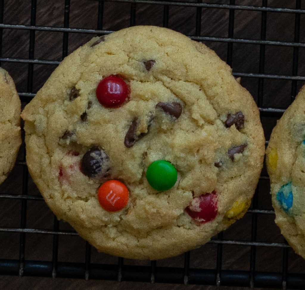 one m&m and chocolate chip cookie on a black cooling rack
