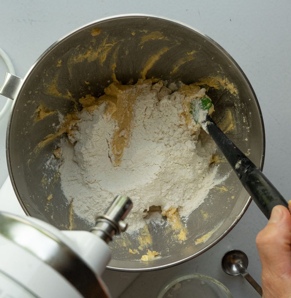 flour added to butter sugar mixture in a silver mixing bowl