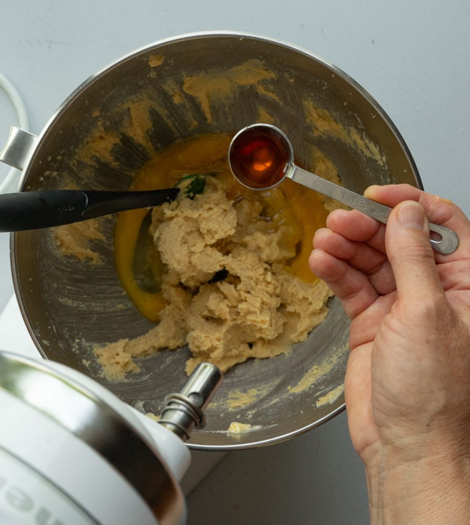 adding vanilla to the sugar butter mixture in a silver mixing bowl
