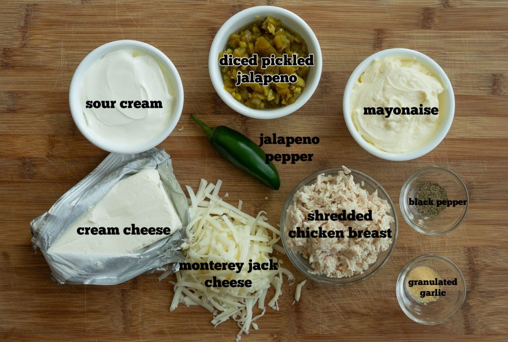 ingredients for jalapeno cheesy chicken dip layed out on a wood cutting board