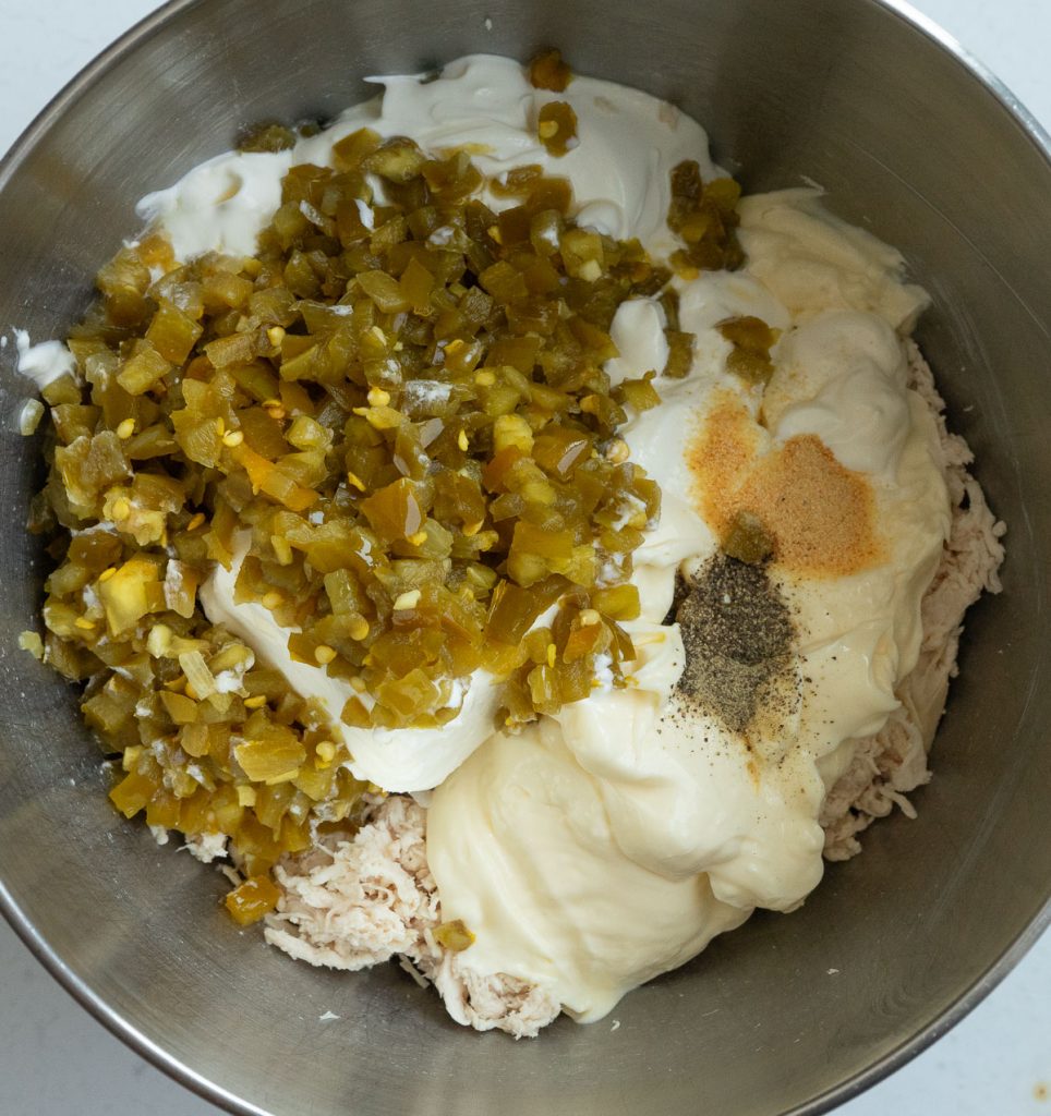 process photo of making the jalapeno cheesy chicken dip folding ingredients into mixture in a stainless steel bowl