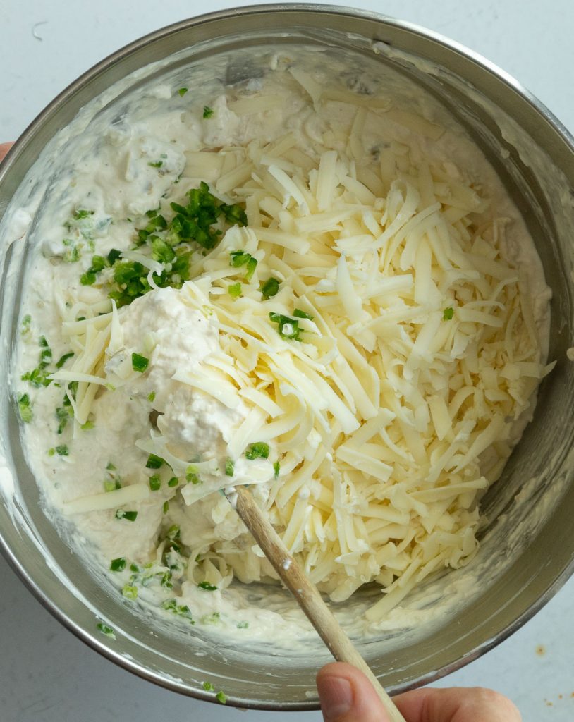 process photo of making the jalapeno cheesy chicken dip folding cheese into mixture in a stainless steel bowl