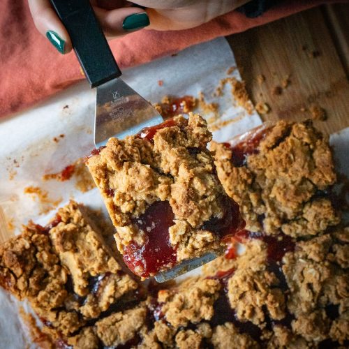 peanut butter and jelly oatmeal bar lifted up by a spatula with pan of bars in the background