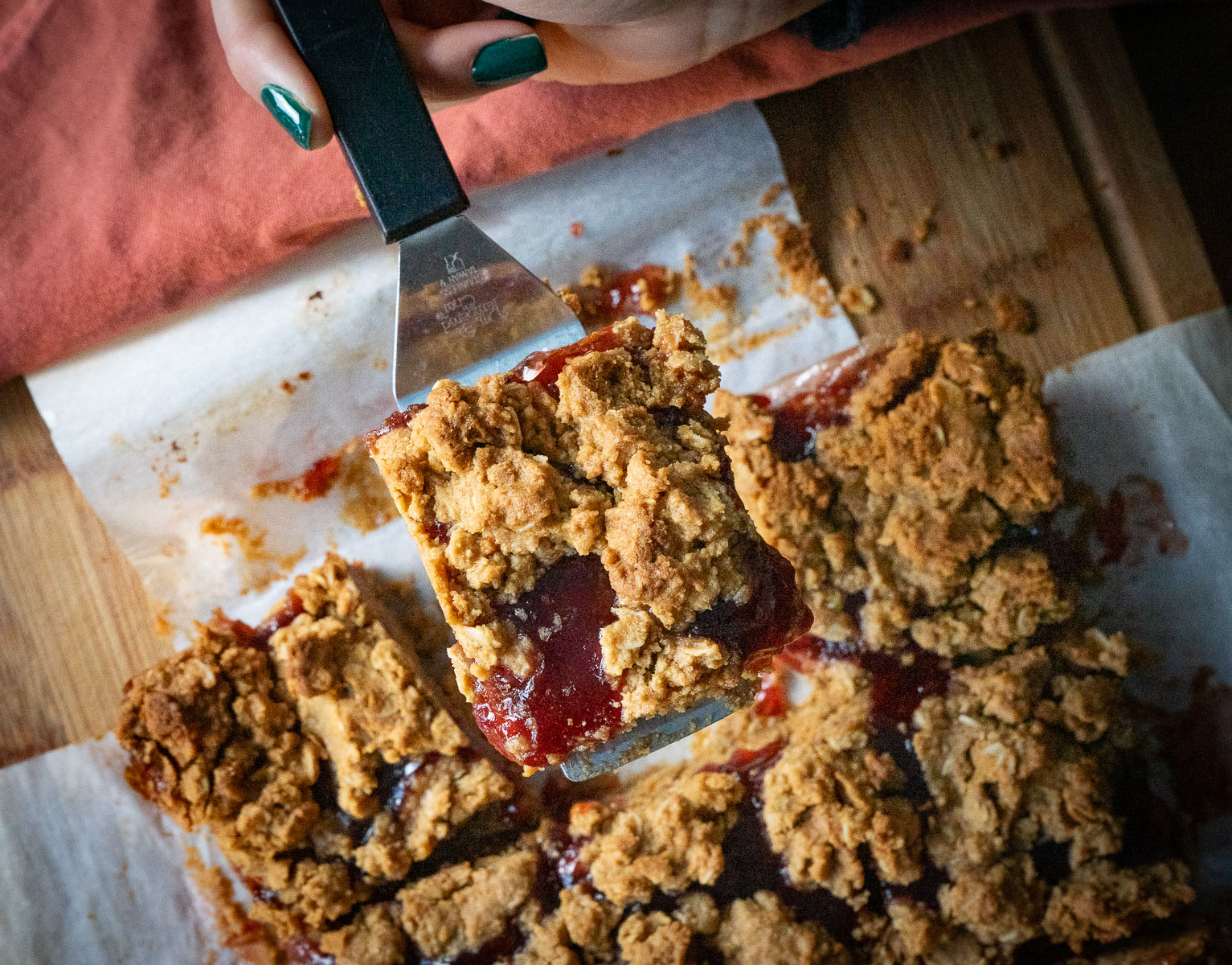 peanut butter and jelly oatmeal bar lifted up by a spatula with pan of bars in the background