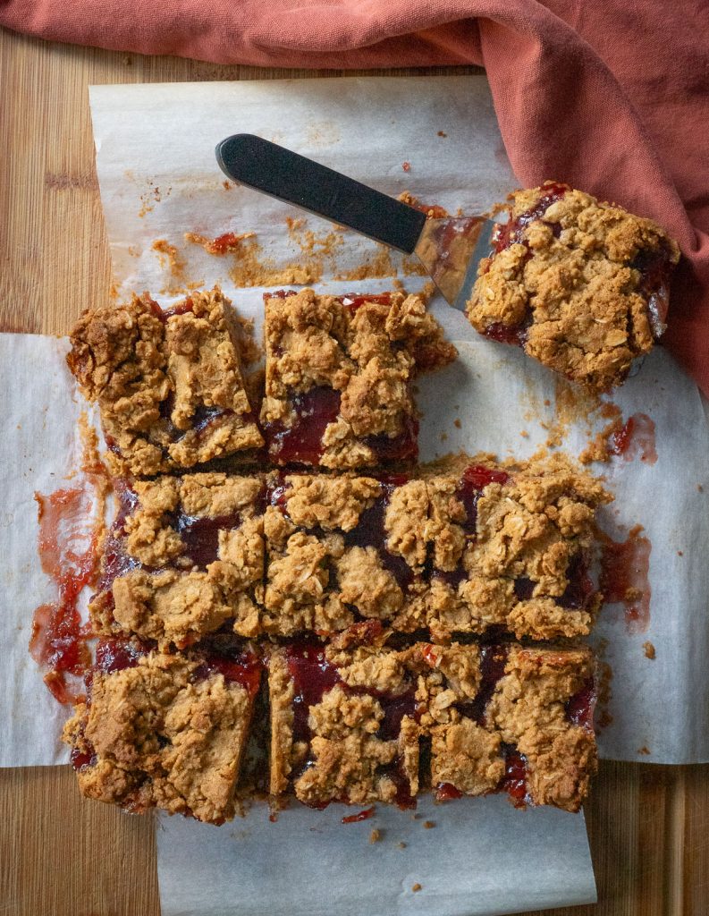 baked peanut butter and jelly bars on parchment paper the corner square is on a spatuala