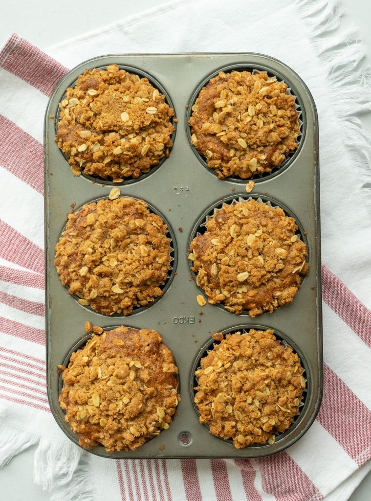 6 large oatmeal breakfast muffins in muffin tin on a red and white kitchen towel