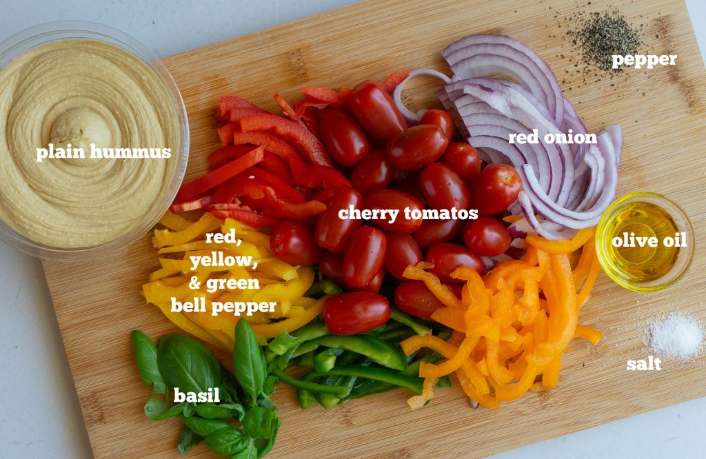 ingredients for roasted vegetables and hummus dip on a rectangle shaped wood cutting board