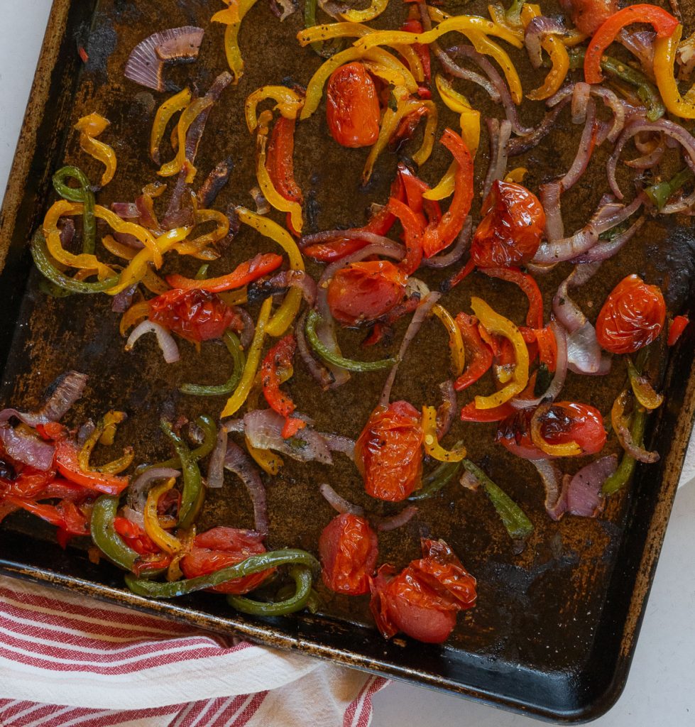 roasted peppers, onions and tomatoes on baking sheet with a red and white striped towel in the background