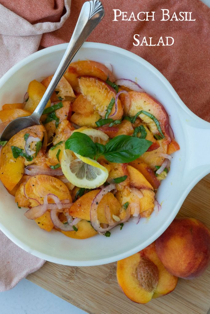 white bowl full of peach basil salad with a silver serving spoon in the bowl on a rust colored towel on a wood countertop