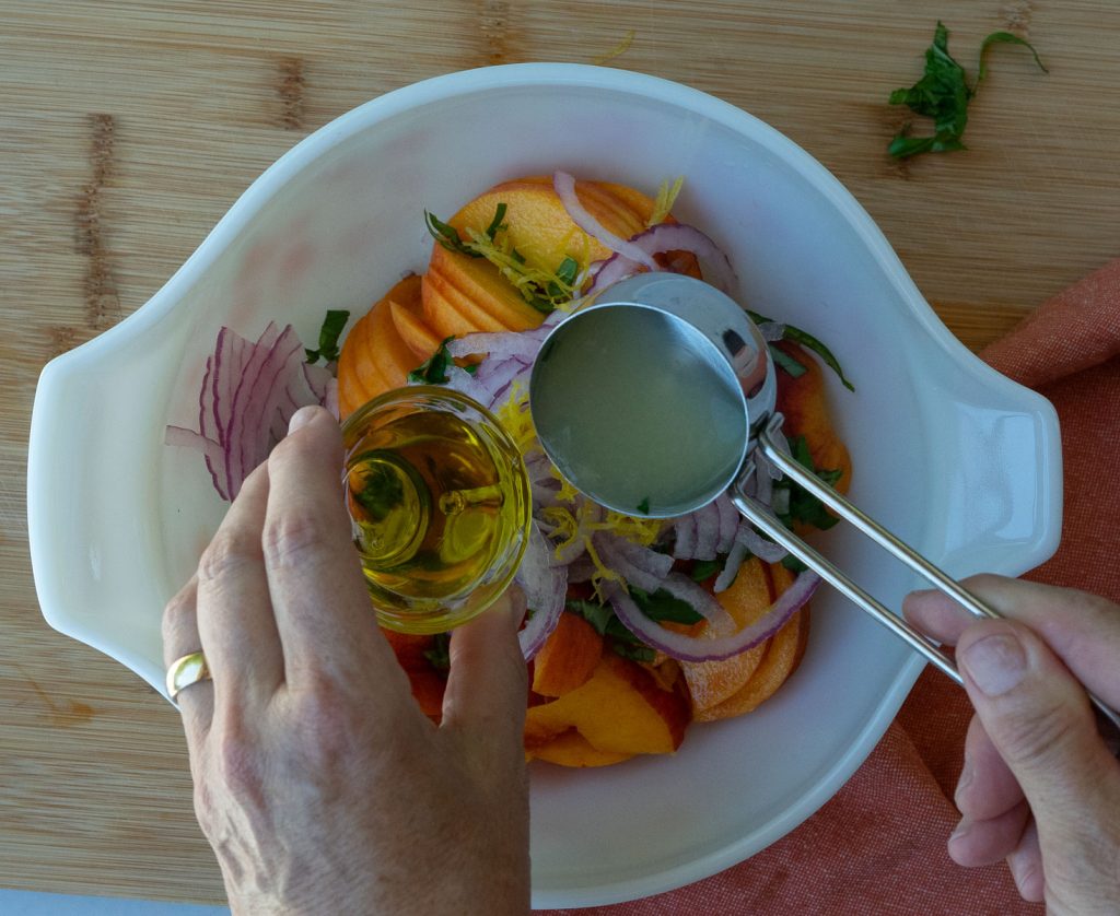 adding lemon juice and olive oil to ingredients in white bowl on a wood cutting board