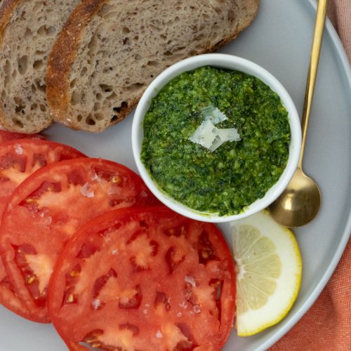 small bowl full of pesto on a plate with crusty bread and sliced tomatoes